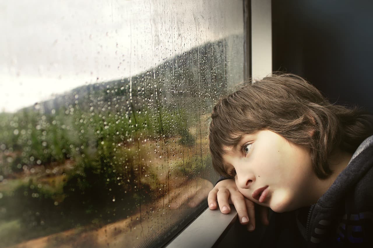 enfant triste près d'une fenetre avec des gouttes de pluie
