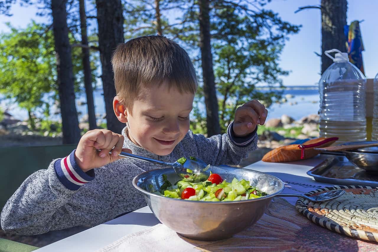 enfant qui mange des légumes sur une tablle de pique nique