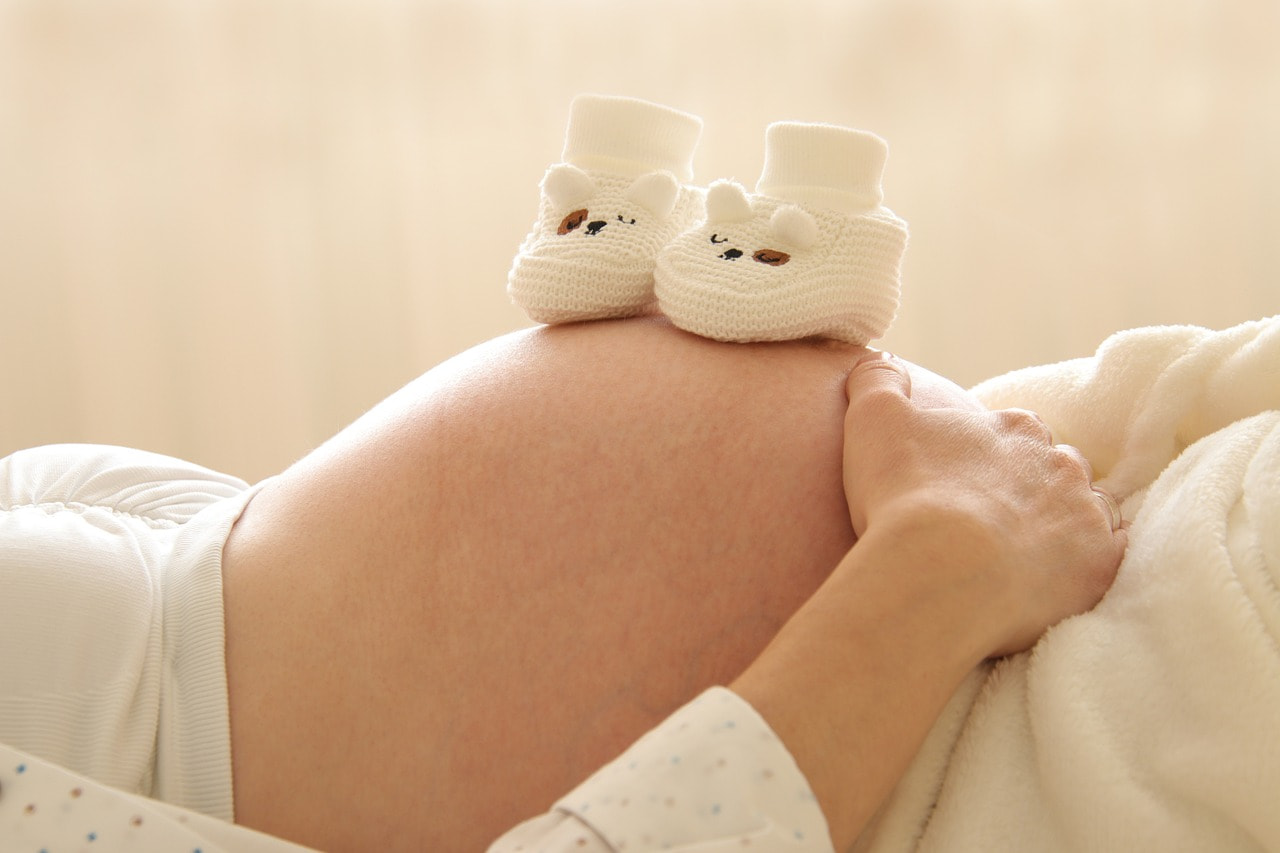 Femme enceinte allongée avec 2 chaussons de bébé sur son ventre