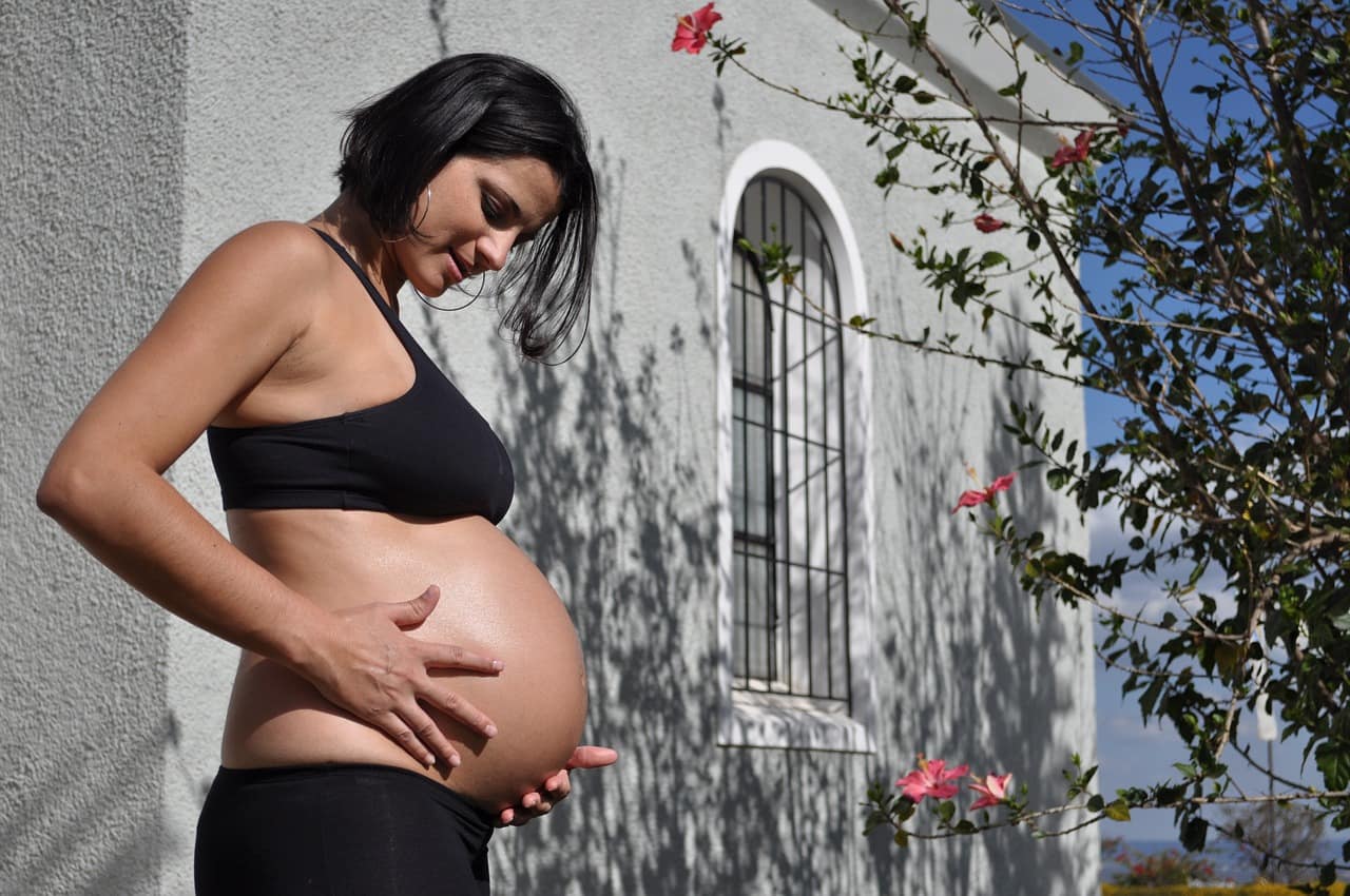 femme enceinte se touchant le ventre en extérieur sous le soleil